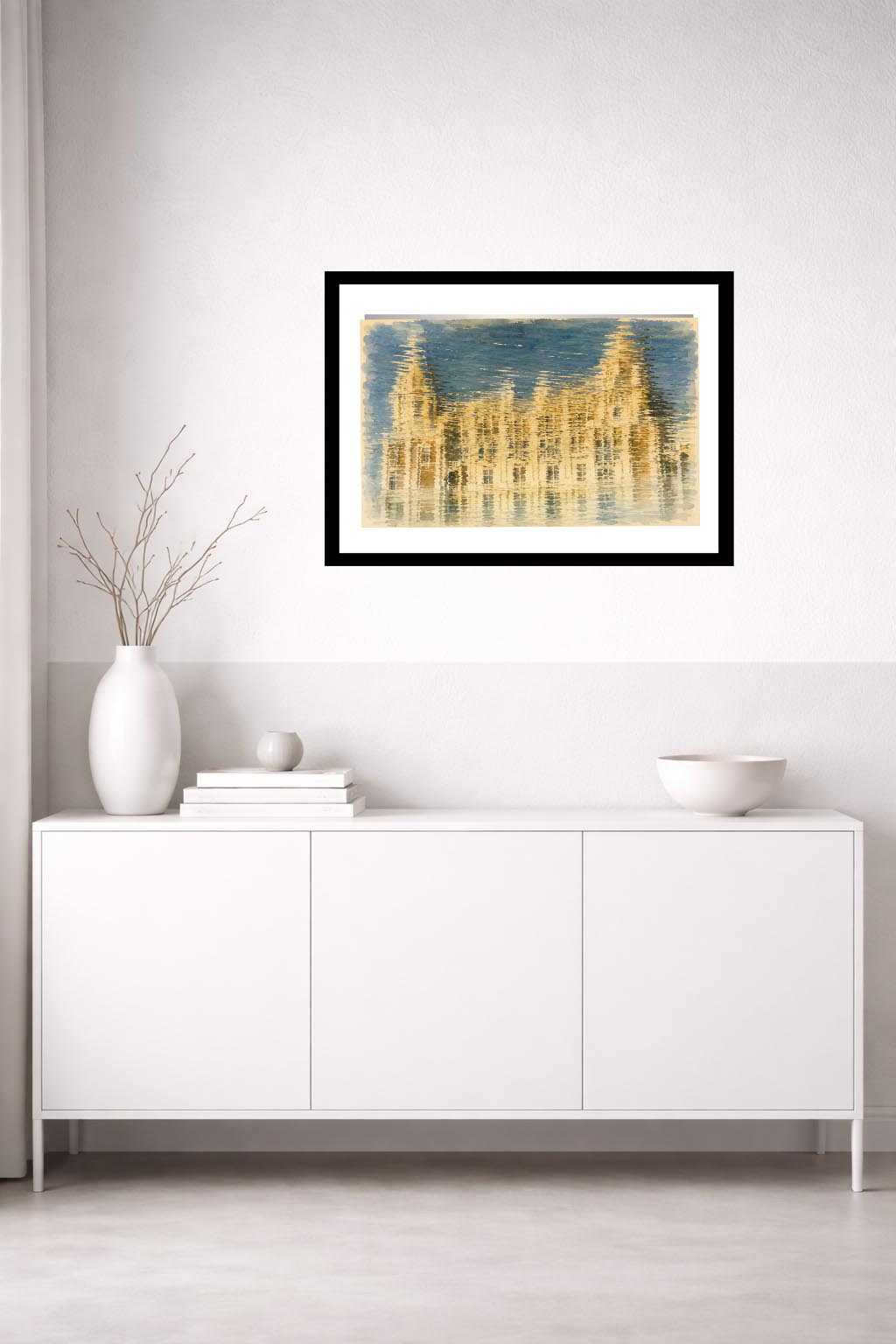 Lámina decorativa Solo Reflejo enmarcada en negro sobre aparador blanco minimalista con jarrones blancos y cuenco, composición abstracta dorada y azul, salón nórdico luminoso