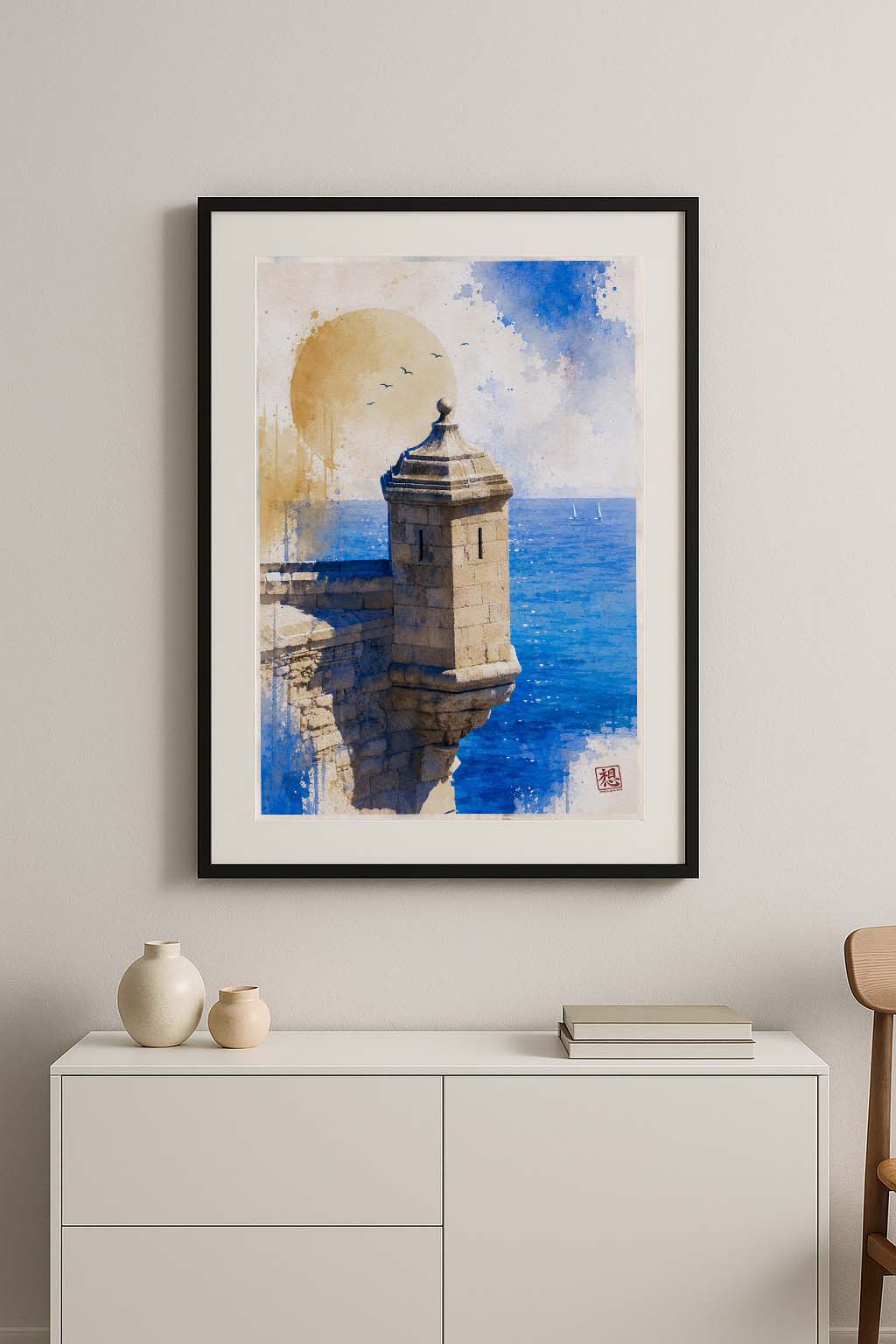 Cuadro enmarcado Torre de Vigilancia sobre aparador blanco lacado con jarrones de cerámica beige y libros, acuarela vertical de garita del Castillo de Santa Bárbara con Mediterráneo azul y sol dorado en ambiente nórdico IMAJIN-ARTE